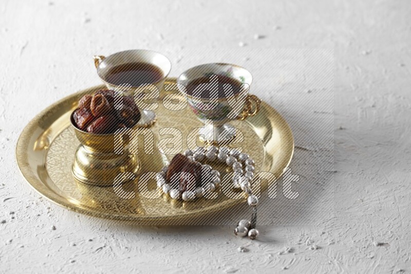 Dates in a metal bowl with tea and prayer beads on a tray in a light setup