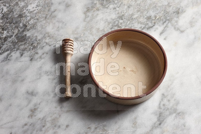 Beige Pottery oven bowl with wooden honey handle on the side with grey marble flooring, 65 degree angle
