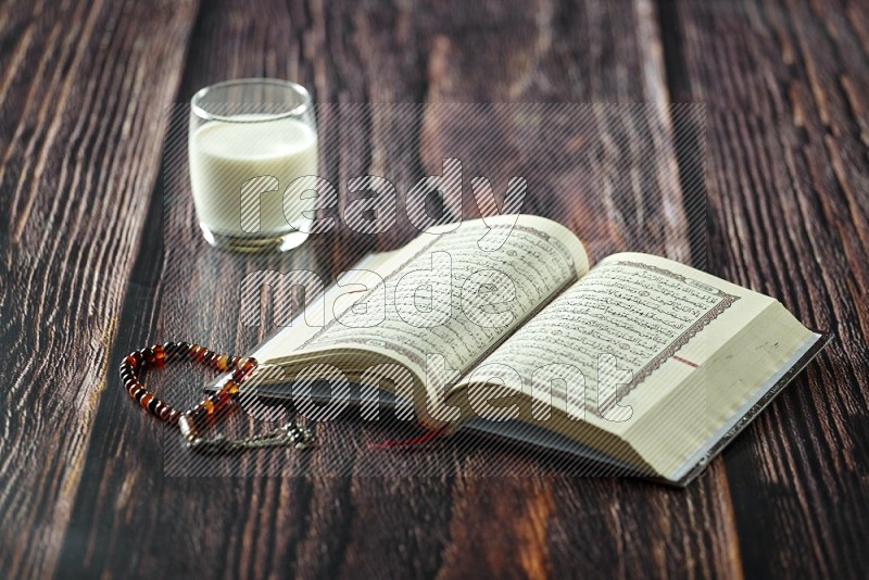 Quran with dates, prayer beads and different drinks all placed on wooden background