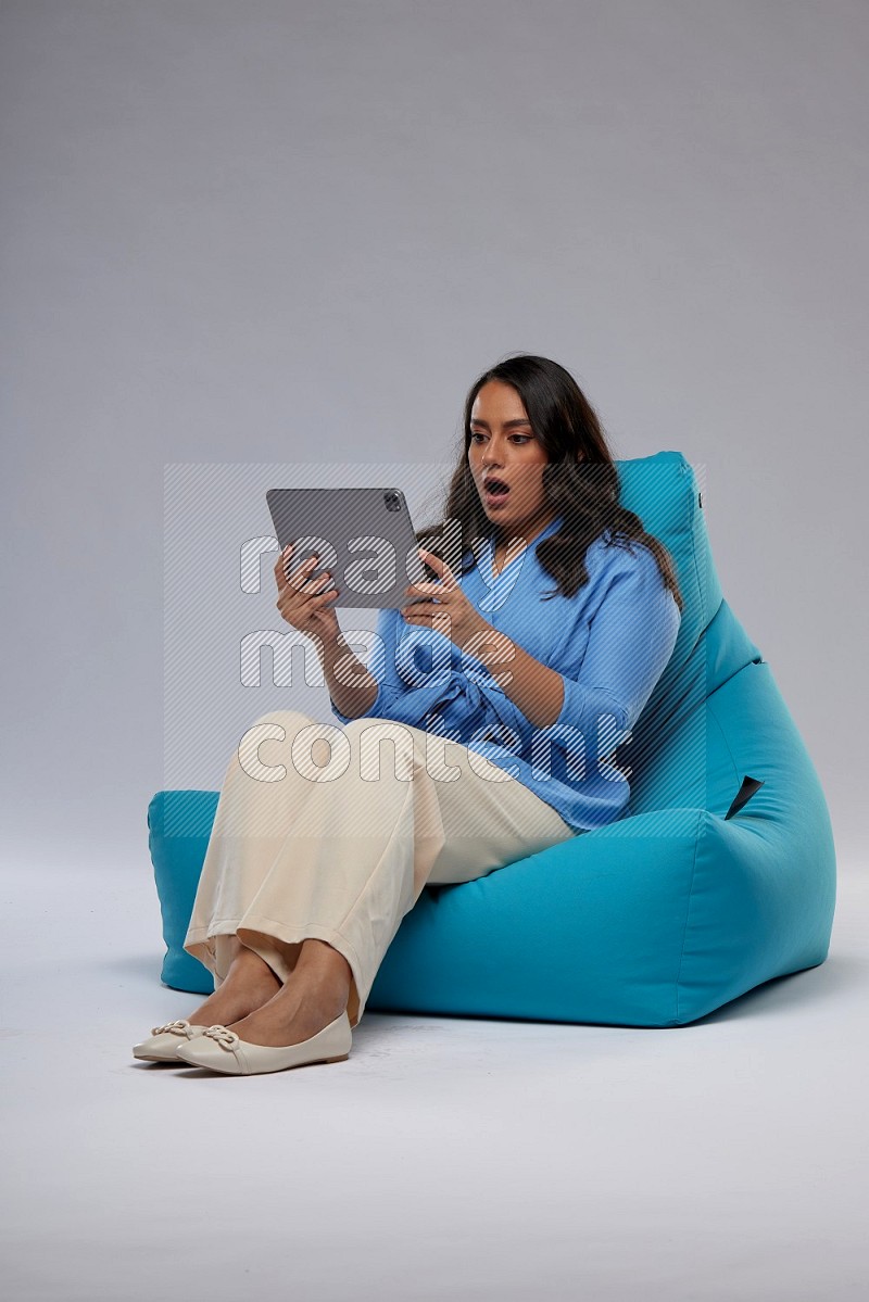 A woman sitting on a blue beanbag and working on tablet