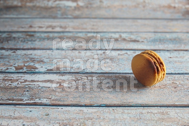 45º Shot of Yellow Crème Brulée macaron on light blue wooden background