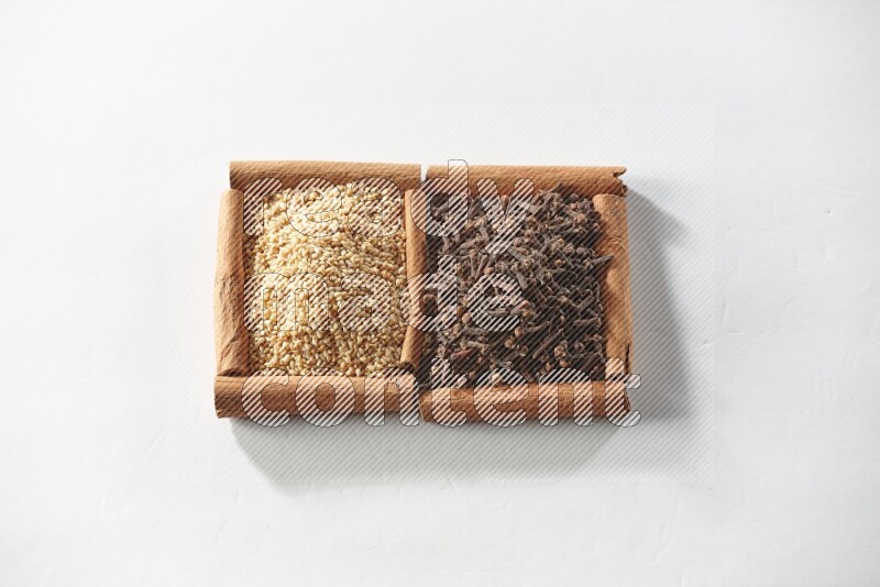 مربعان من أعواد القرفة ممتلئان بالقرنفل وبذور السمسم علي خلفية بيضاء