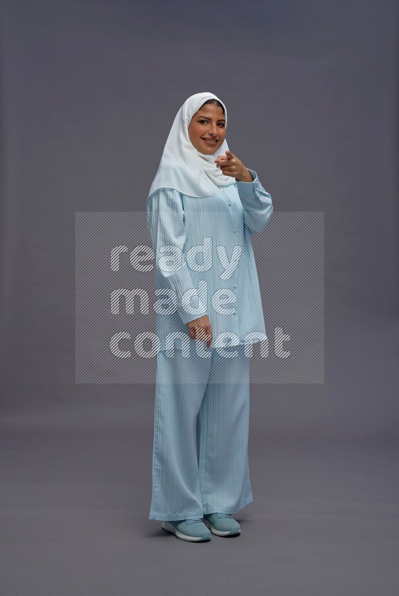 Saudi woman wearing hijab clothes standing interacting with the camera on gray background