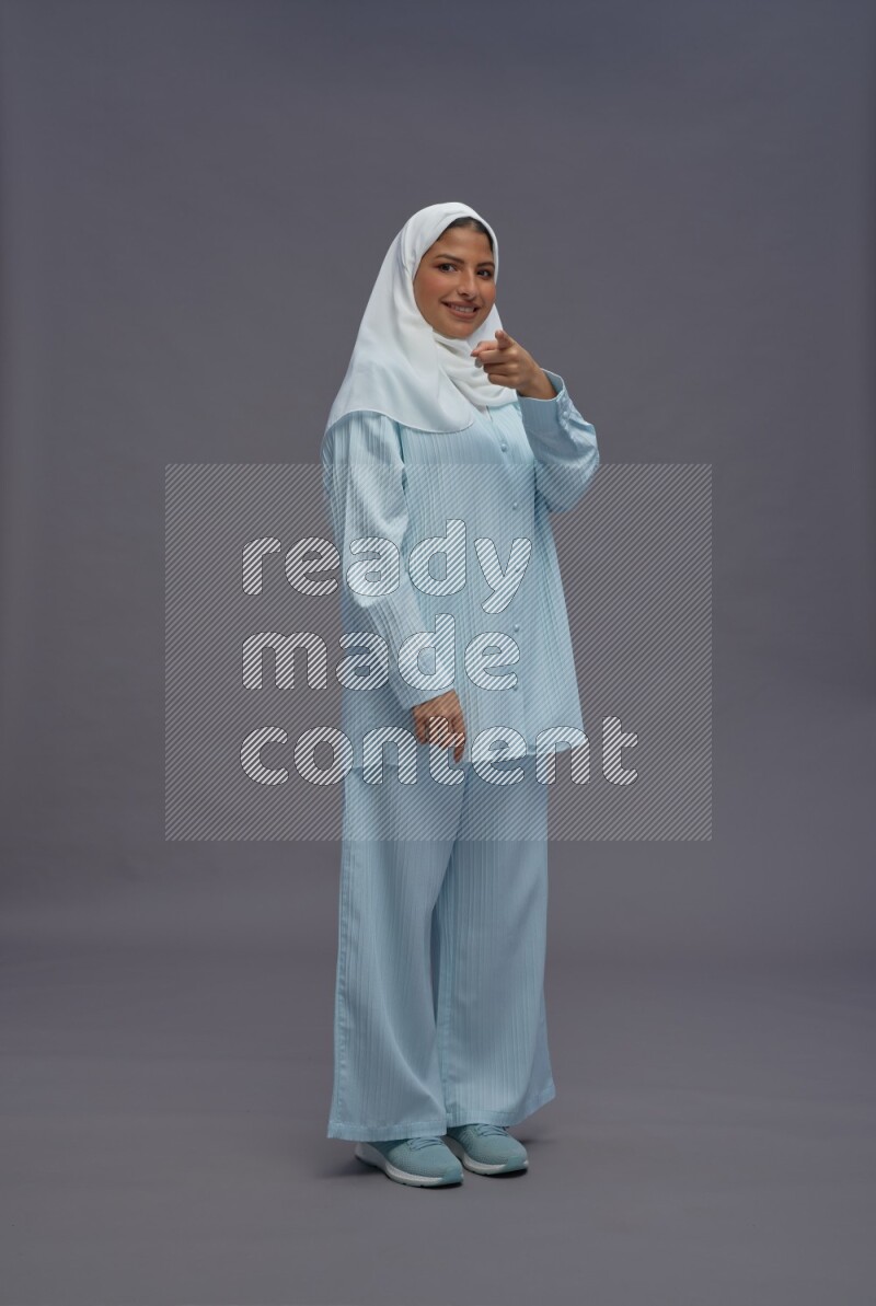 Saudi woman wearing hijab clothes standing interacting with the camera on gray background