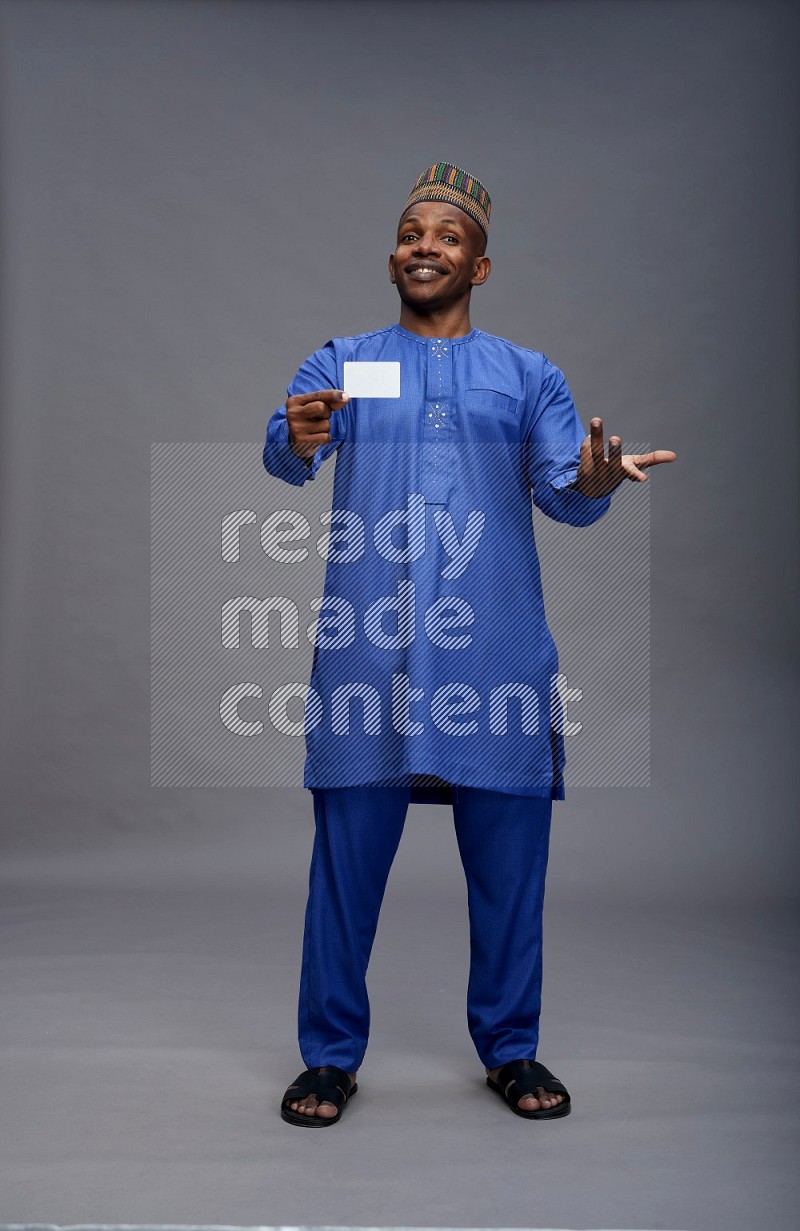 Man wearing Nigerian outfit standing holding ATM card on gray background