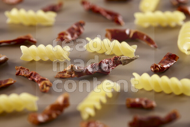 Raw pasta with different ingredients such as cherry tomatoes, garlic, onions, red chilis, black pepper, white pepper, bay laurel leaves, rosemary and cardamom on beige background