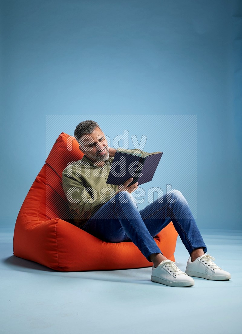A man sitting on an orange beanbag and reading a book