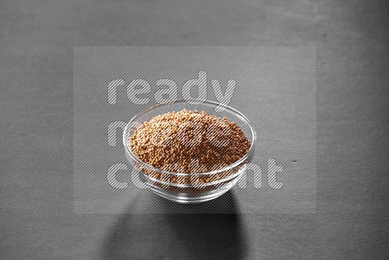 A glass bowl full of mustard seeds on black flooring