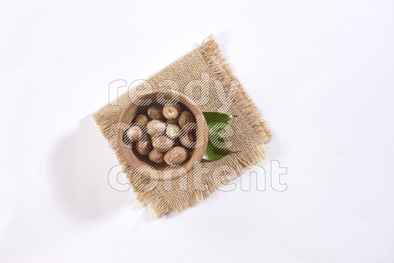 A wooden bowl full of nutmeg on burlap fabric on a white flooring in different angles