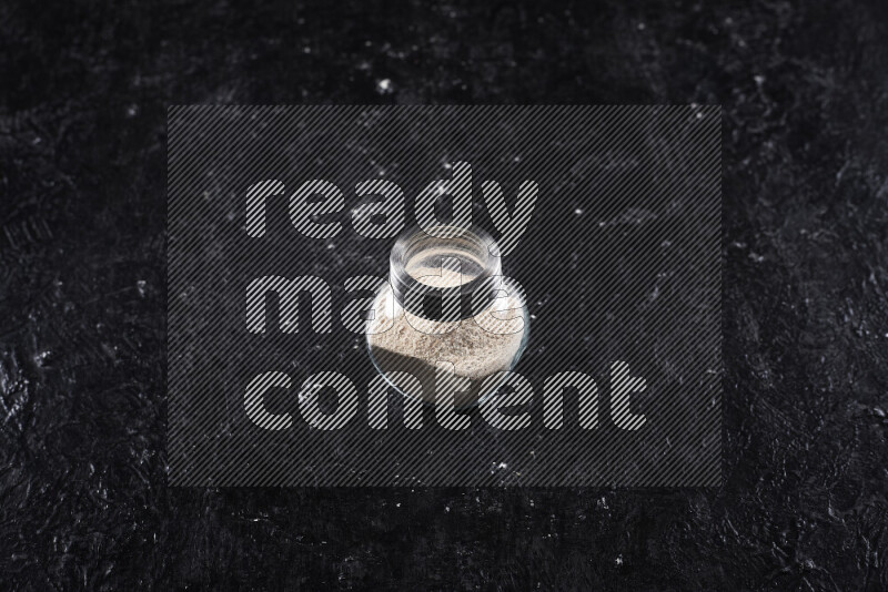 A glass jar full of onion powder on black background