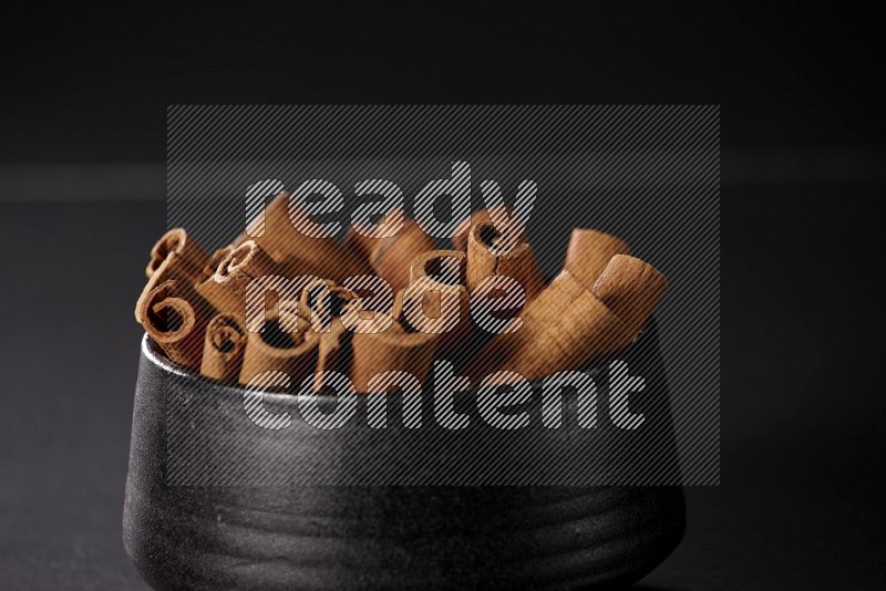 Cinnamon sticks in a black bowl on a black background in different angles