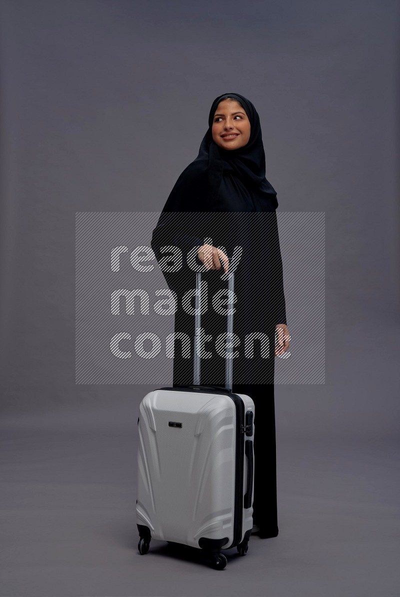 Saudi woman wearing Abaya standing holding bag on gray background