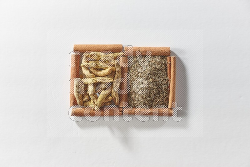 مربعان من أعواد القرفة ممتلئان بحبوب الكمون وأصابع الكركم علي خلفية بيضاء