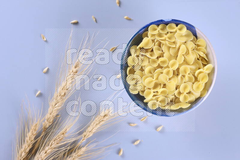 Raw pasta with wheat stalks on light blue background