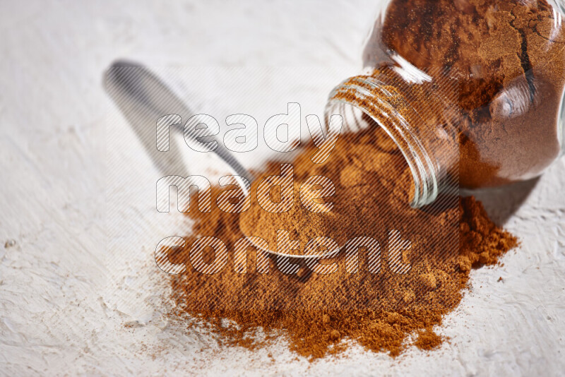 A glass jar full of ground paprika powder flipped with some spilling powder on white background