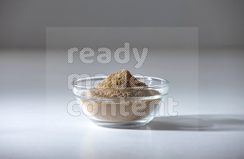 A glass bowl full of cumin powder on a white flooring