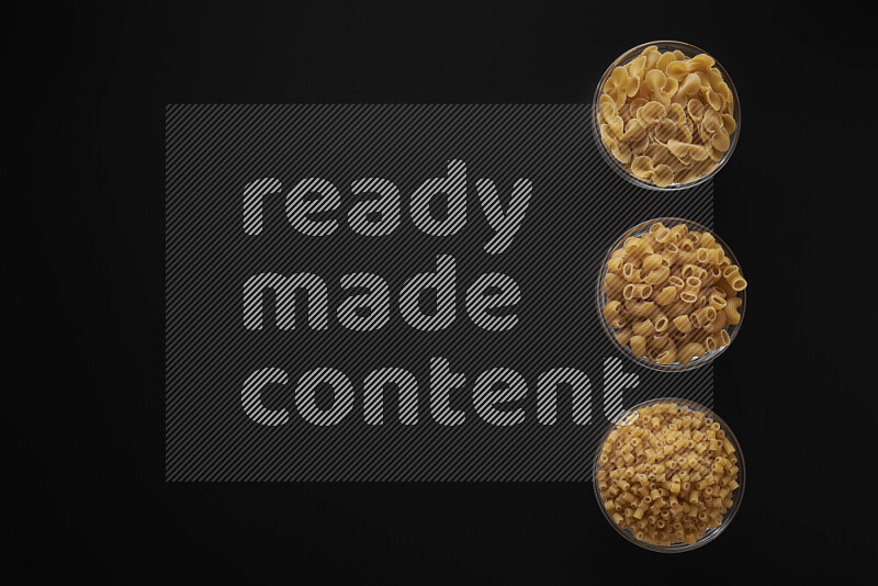 Different pasta types in 3 glass bowls on black background