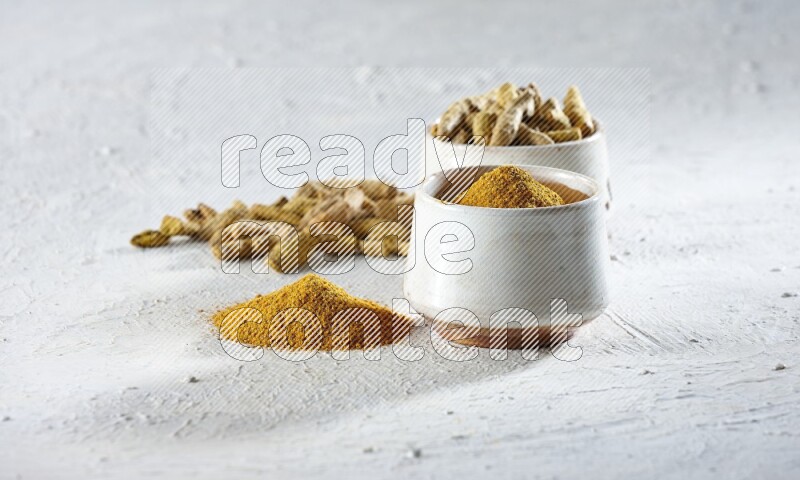 2 beige pottery bowls full of turmeric powder and dried turmeric whole fingers with powder and fingers next of it textured white flooring