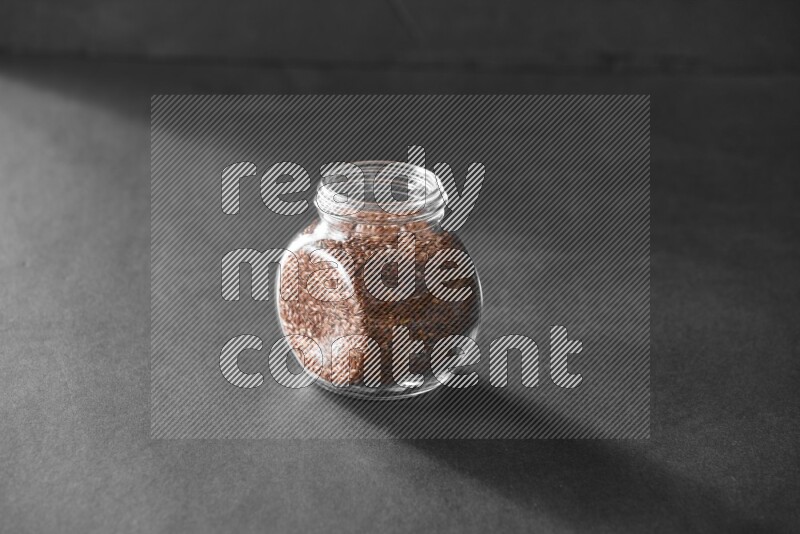 A glass spice jar full of flax on black flooring