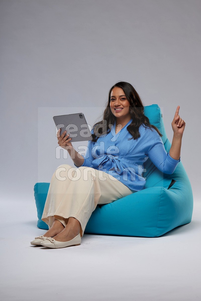 A woman sitting on a blue beanbag and working on tablet