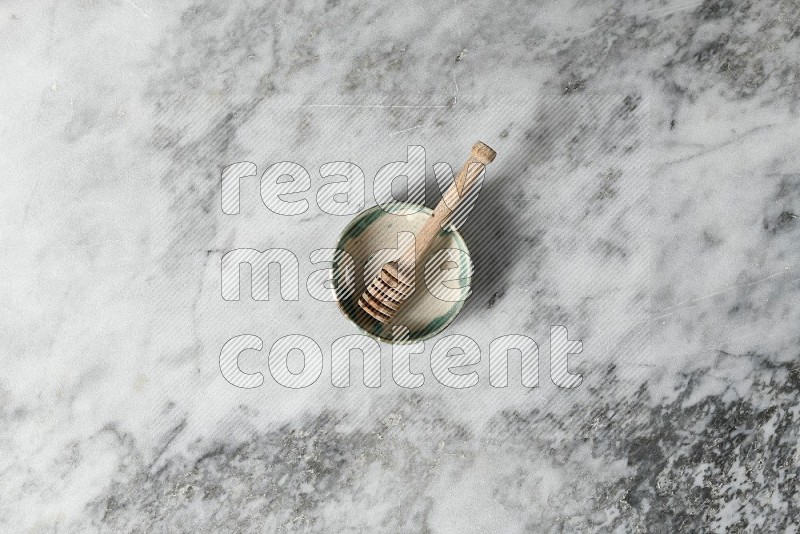 Multicolored Pottery Bowl with wooden honey handle in it, on grey marble flooring, Top View