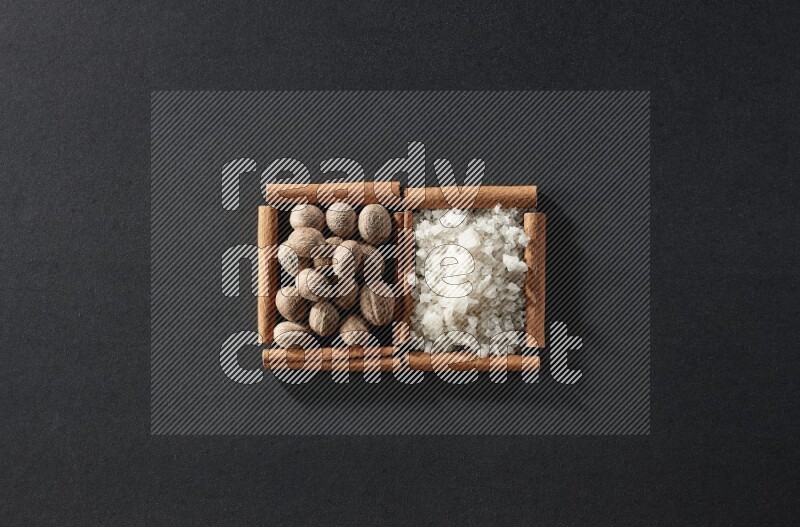 مربعان من أعواد القرفة ممتلئان بجوزة الطيب والملح الأبيض علي خلفية سوداء