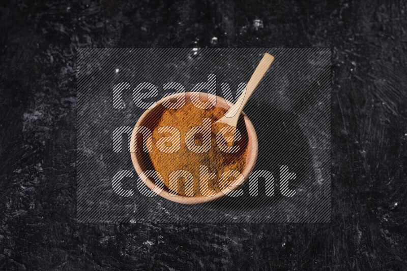 A wooden bowl full of ground paprika powder and a wooden spoon in it on black background