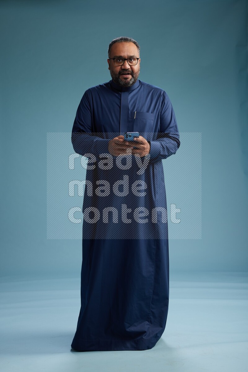 Saudi Man without shimag Standing texting on phone on blue background