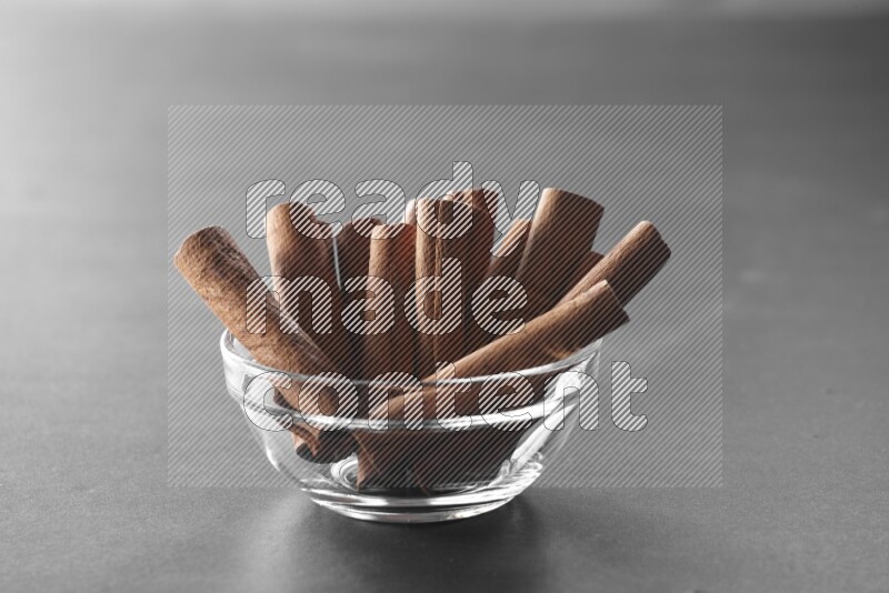 A glass bowl full of cinnamon sticks on black flooring