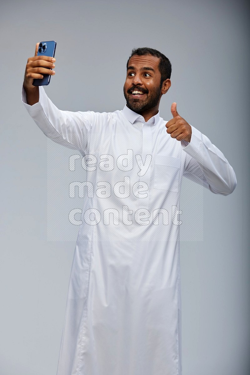 Saudi man wearing Thob standing taking selfie on Gray background