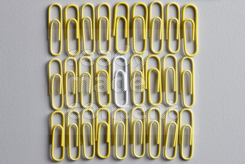 A white paperclip surrounded by bunch of yellow paperclips on grey background