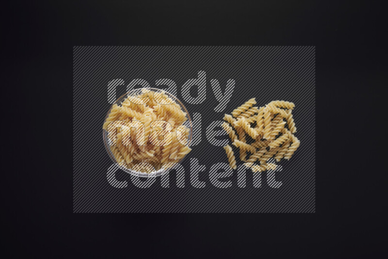Fusilli pasta in a glass bowl on black background