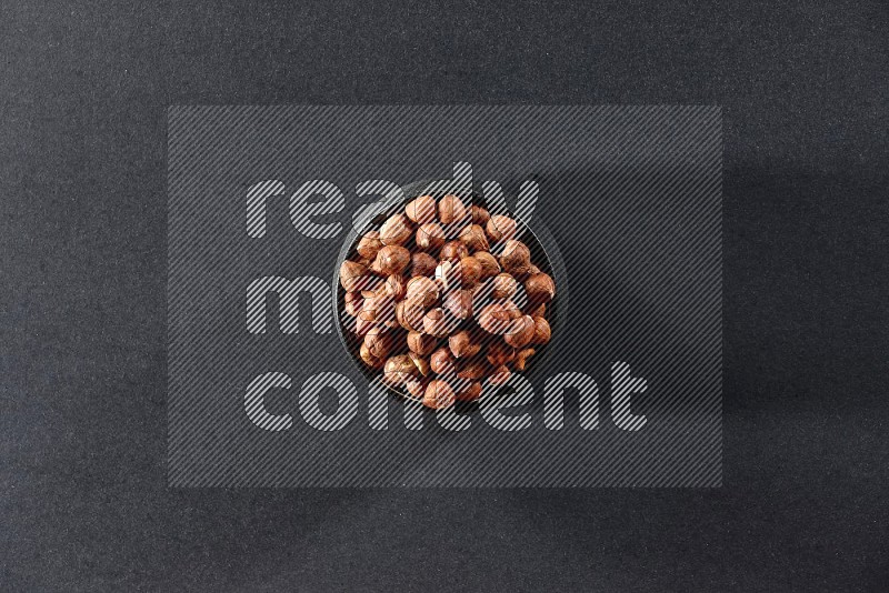 A black pottery bowl full of peeled hazelnuts on a black background in different angles