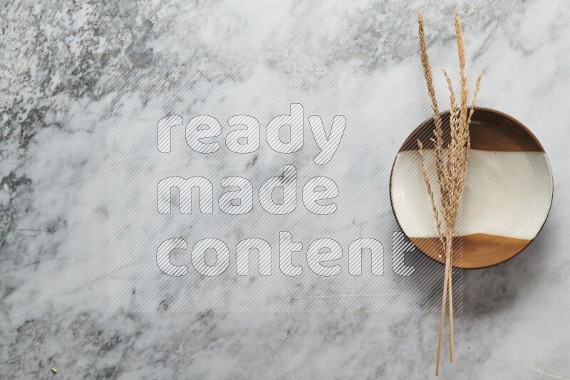 Wheat stalks on multicolored pottery plate on grey marble background