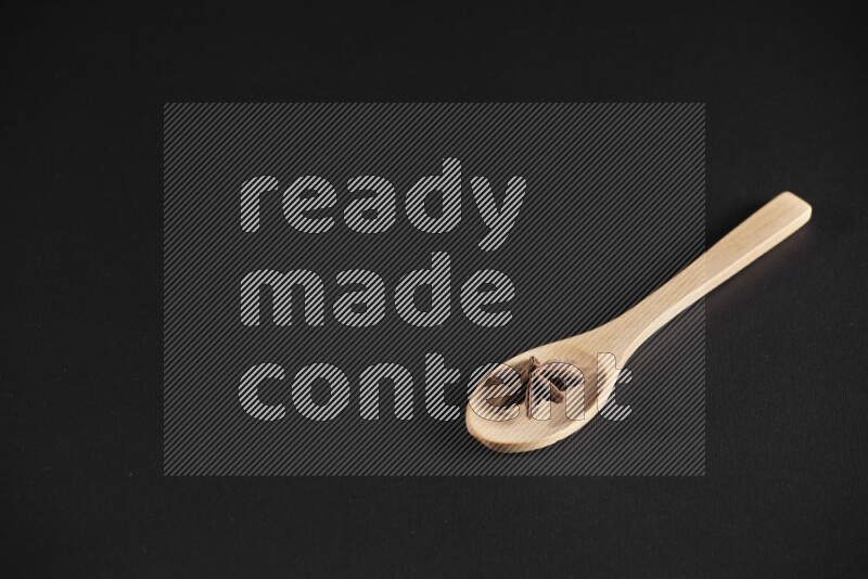 اليانسون النجمي في ملعقة خشبية فوق اليانسون النجمي الذي يغطي الإطار على أرضية سوداء