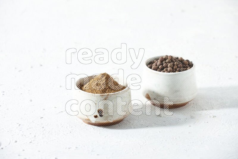 وعاءان بيج، أحدهما ممتلئ ببودرة بهار الفلفل الحلو والآخر بحبوبه، على خلفية بيضاء