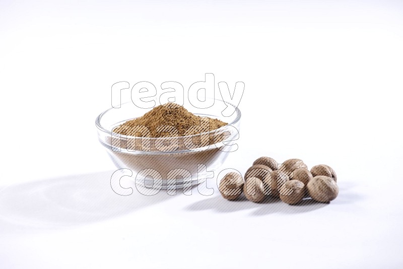 A glass bowl full nutmeg powder with the seeds beside it on a white flooring in different angles