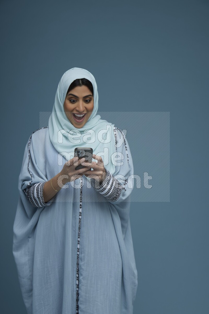 A Saudi woman Texting in a blue background wearing a blue Abaya with hijab