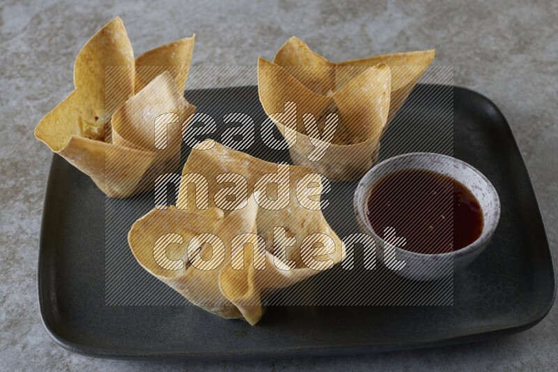 wonton cups with soy sauce ramkin on rectangle dark grey ceramic plate on grey textured counter top