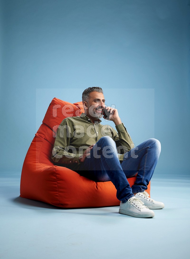 A man sitting on an orange beanbag and talking on the phone