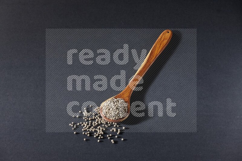 A wooden ladle full of white pepper beads on black flooring