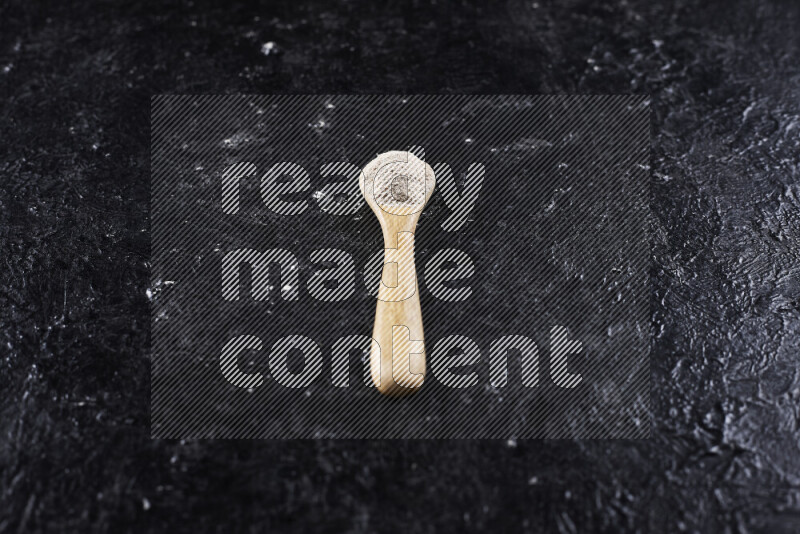 A wooden spoon full of onion powder on black background