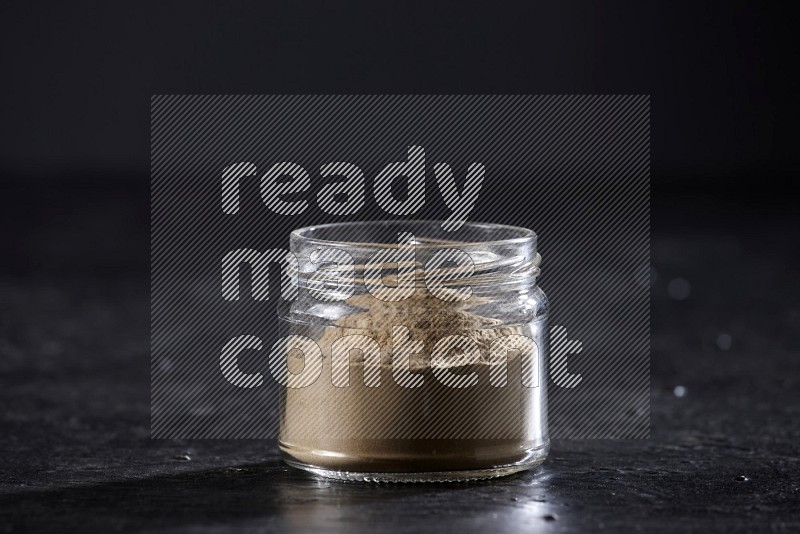 A glass jar full of garlic powder on a textured black flooring in different angles