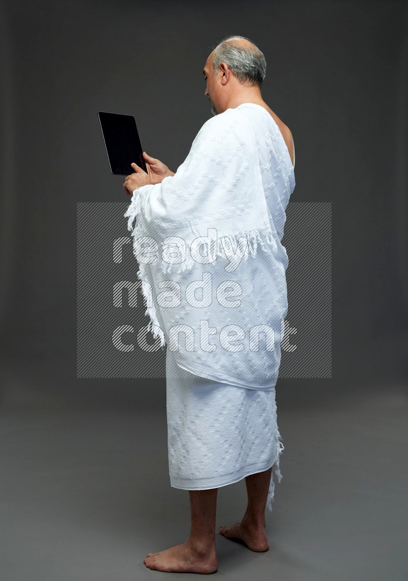A man wearing Ehram Standing working on tablet on gray background