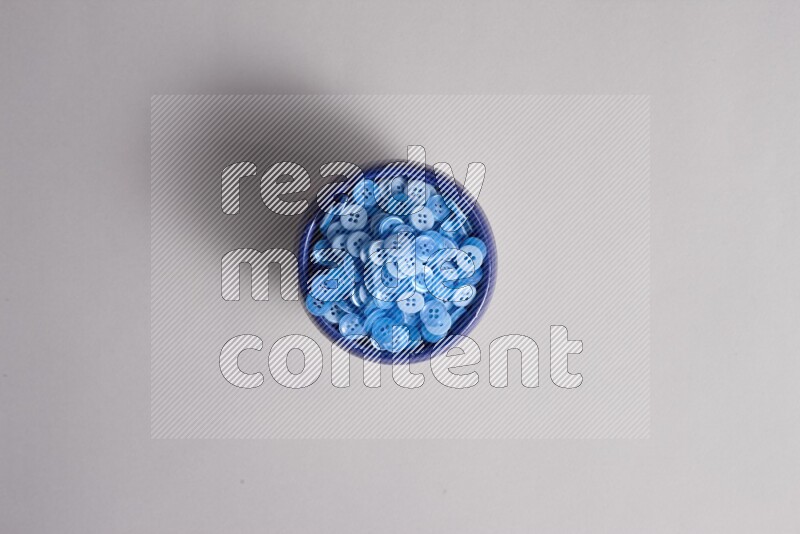 A multicolored pottery bowl full colored buttons on grey background