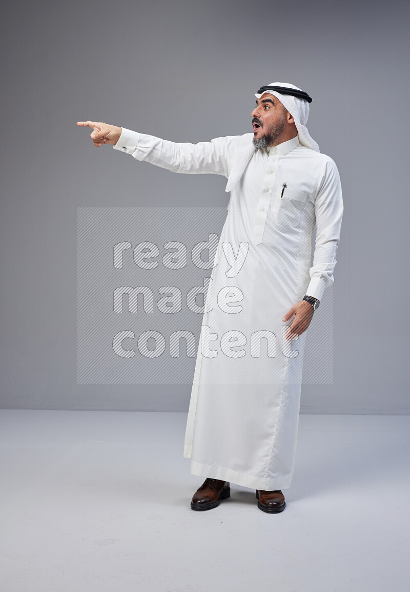 Saudi man Wearing Thob and white Shomag standing interacting with the camera on Gray background