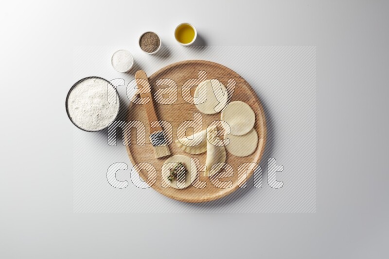 two closed sambosas and one open sambosa filled with meat while flour, salt, black pepper and oil with oil brush aside in a wooden dish on a white background