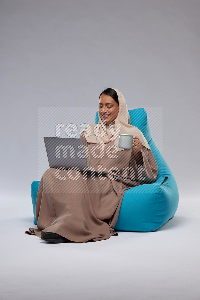 A Saudi woman sitting on a blue beanbag and working on laptop