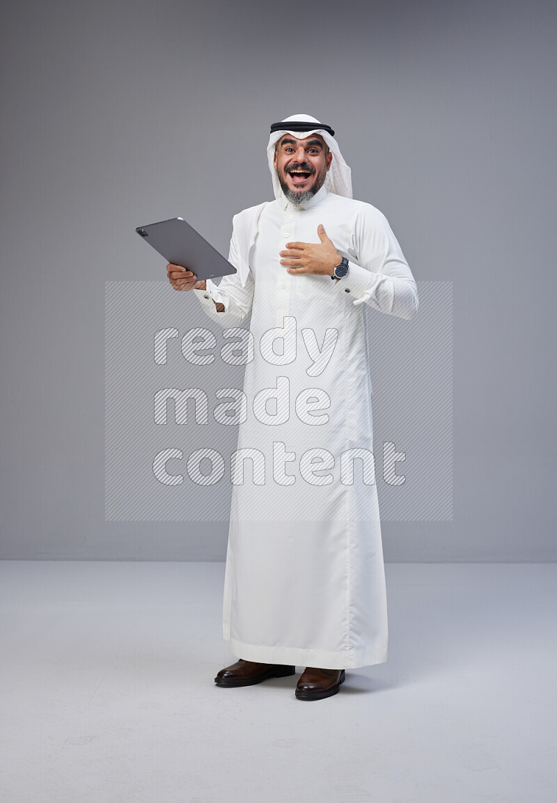 Saudi man Wearing Thob and white Shomag standing working on tablet on Gray background