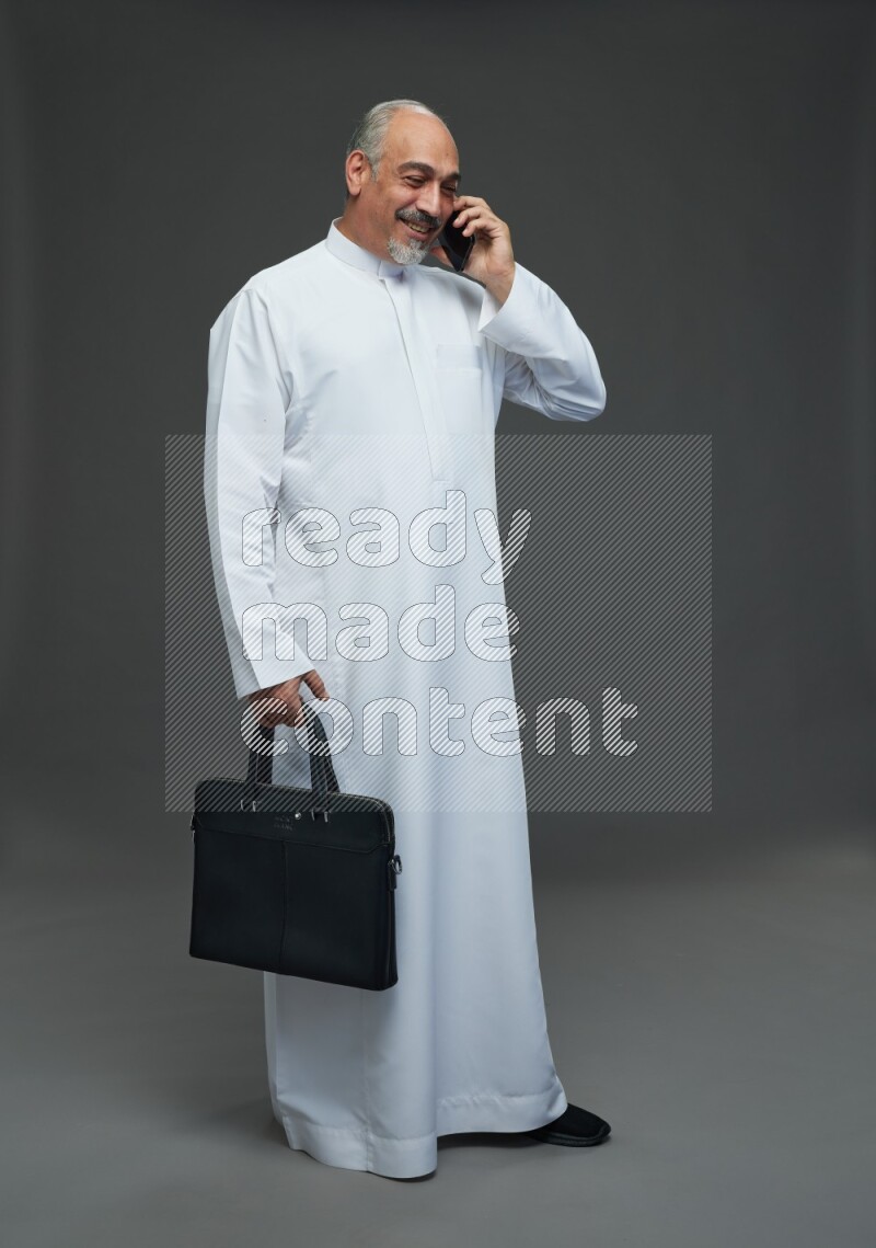 Saudi man without shomag Standing holding bag and talking on phone on gray background